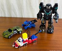 Group shot showing Optimus Prime truck, green car, blue car with accessory, large black robot
