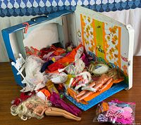 Open blue Barbie case showing two dolls, piles of clothing, hangers and accessories