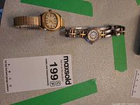 Two wrist watches laid on surface with lot tag for scale