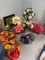Group of silk flowers, garland, purple ornament balls, glass vase and some frames visible