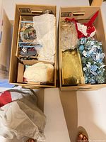 Two cardboard boxes with various holiday decorations and wrap supplies