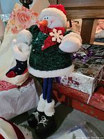 Snowman plush figure standing among gift wrap items