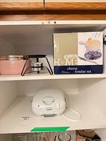 Shelf with fondue set components and box above sandwich maker