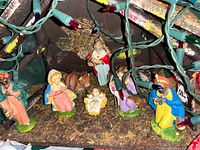 Resin nativity figures inside wooden stable with string lights draped over