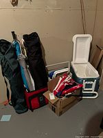 Lot overview showing Igloo cooler open, two folding chair bags, umbrellas, red soft bag, cardboard box with accessories