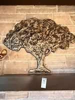 Full view of metal tree wall sculpture on shelf against brick wall