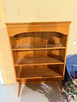 Front view of light brown wood bookcase with three shelves and brass-tone rail