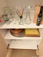 Group view of jars, vases, diffuser, olive-oil bottle and gift bag on cabinet shelf
