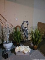 Group shot showing heron sculpture, two grass planters, urn with faux tree, wood planter with flowers