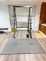 Front view of power/squat rack with J-cups, coil of cable, pump on floor, mats in foreground