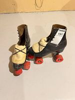 Pair of black quad skates standing, showing uppers, tongue covers, wheels