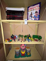 Shelf view showing Rubik’s Cubes, action figures, dinosaur figures, John Deere tractor & trailer, castle playset base