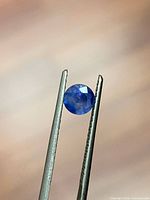Round blue sapphire held by tweezers showing color and cut