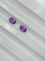 Two oval purple gemstones on white surface