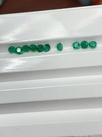 Row of ten vivid green round emeralds on white tray