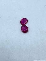 Two oval-cut red rubies on white background