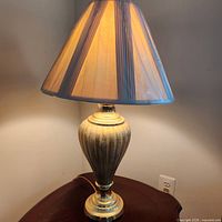 Full view of one brass-finish table lamp with pleated shade on tabletop, illuminated