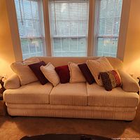 Full view of beige patterned sofa with throw pillows in front of windows