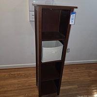 front view of tall dark brown bookshelf with fabric bin on middle shelf