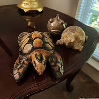 Three figurines on table: wood turtle, stone puffer fish, soapstone turtle