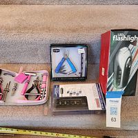 All four items displayed: open pink tool kit, boxed blue multitool, boxed LED flashlight, carded USB car charger