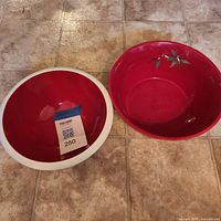 Two ceramic serving bowls on tile floor, red interior white rim bowl and red bowl with cherry motif