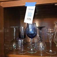 Shelf with eight assorted stemmed glasses in clear, blue, purple and smoky colors, some upright, some inverted