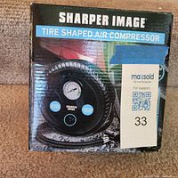 Front of Sharper Image Tire Shaped Air Compressor box showing product image and gauge