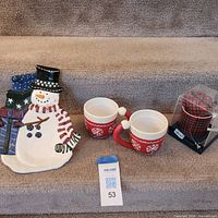 Group shot of snowman plate, two red mugs, boxed plaid mug & tie