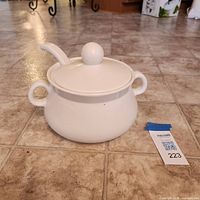 White ceramic soup tureen with lid and ladle on tiled floor