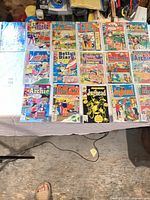 Tabletop view of approximately 18 Archie-related comic books laid out in four rows