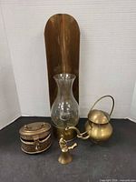 Group view of all four brass items: wall sconce with glass shade, oval trinket box, watering can, bell