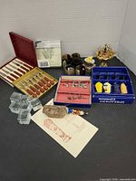 Overall lot view showing all boxed utensils, napkin rings, place card holders, carving set, sword pick stand and bread basket figure