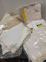 Stack of embroidered napkins, packaged napkins, lace pieces, sheer embroidered topper