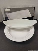 Three platters shown together: oval with handles atop Corning round platter; Toscana boxed platter in background