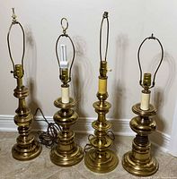 Four brass table lamps with cords, harps and sockets visible