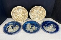 Five collector plates displayed, three blue cameo and two ivory relief