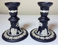 Front view of both black jasperware candlesticks showing white relief decoration.