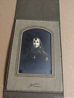 Full view of mounted photograph showing nun in habit with cross within arched matte folder
