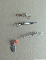 Three lures laid out: brass-tone spoon, hammered silver spoon, wire spinnerbait
