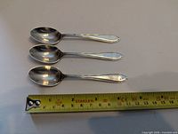 Three matching silver plate dessert spoons next to measuring tape