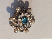 Front view of brooch showing blue centre stone, clear rhinestones, faux pearls and gold-tone floral design