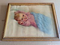 Full view of framed lithograph showing baby in pink sweater under blue blanket