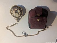 Pocket watch with chain beside leather pouch