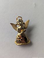 Front view of gold tone angel brooch showing white enamel wings and red poinsettia detail