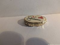 Closed oval sewing kit showing lid artwork and metal casing