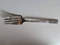 Full view of silver plate serving fork showing four tines and ornate handle pattern