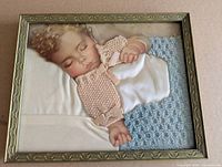 Front view of framed Charlotte Becker baby lithograph collage with lace, satin, knitted and crocheted textile accents