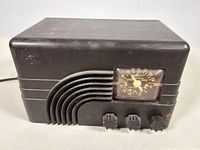 Front angled view of Bakelite radio showing cabinet, grille, knobs and power cord
