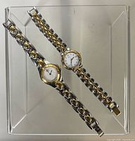 Both watches full view on acrylic stand showing design, bracelet style and two-tone finish